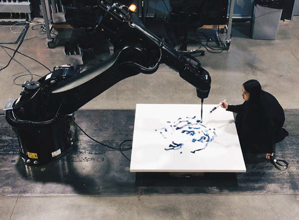 Die amerikanisch-kanadische Künstlerin Sougwen Chung arbeitet zusammen mit einer selbst trainierten KI, einem Roboter, der ihre Malgeste in einer gemeinsamen Malperformance multipliziert und wiedergibt. Sougwen Chung, Drawing Operations, 2017, Performance © obvious-art.com