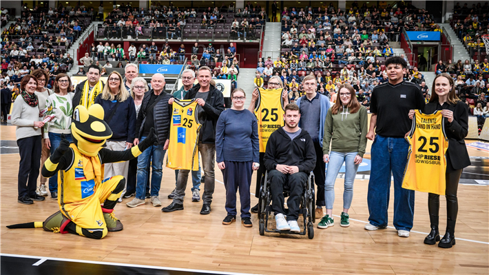 Nachwuchsathleten der Porsche BBA, Inklusionsspieltag der MHP RIESEN, Talente Hand in Hand, 2025 - Mittig, mit Trikot-Vorderseite: Hergen Blase, Geschäftsführer LudwigsTafel e.V.; daneben: ehrenamtliche Mitarbeiter der LudwigsTafel; dahinter mit Trikot: Martina Tetz, Geschäftsbereichsleiterin Ausbildungszentrum Karlshöhe; daneben: Auszubildende der Karlshöhe.© Porsche AG