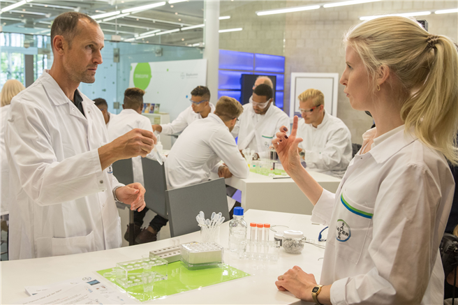 Baylab-Mitarbeiterin Julie Lütten erläutert Trainer Heiko Herrlich, wie man seine eigene DNA extrahiert. © Bayer AG