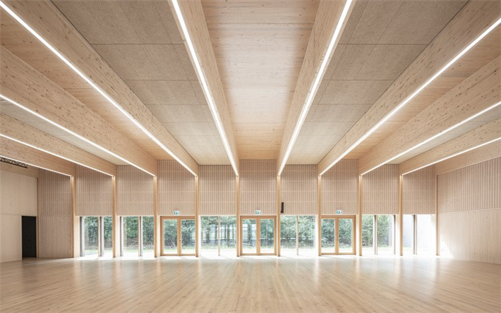 Im Inneren der Kulturhalle dominieren helle Sichtholzflächen, der Blick schweift durch die fast gebäudebreite Glasfront in den direkt angrenzenden Bienwald. ©: AV1 Architekten GmbH, Kaiserslautern
