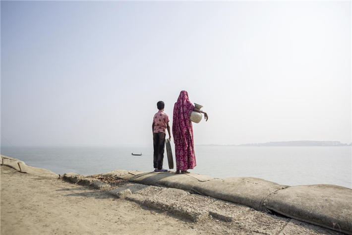 Nasima Khatun und ihr Kind stehen stellvertretend für Tausende von klimabedrohten Gemeinschaften, die im Küstengürtel von Bangladesch leben. Zusätzlich zu ihrer Belastung durch die Auswirkungen der Klimakrise verbringen sie einen großen Teil ihrer Zeit und Arbeit mit der Beschaffung von Frischwasser, um ihre Grundbedürfnisse zu decken. Dieses Foto verdeutlicht die geschlechtsspezifischen Auswirkungen der Wasserkrise, da es oft Frauen und Kinder sind, die die Last des Wasserholens für ihre Familien tragen. © Jahangir Alam/Oxfam in Bangladesch